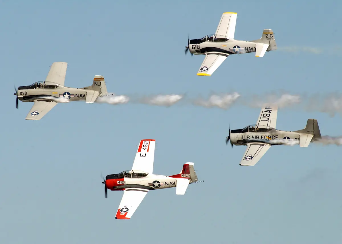 Four T-28 Trojan warbirds in formation with smoke trails at an air show